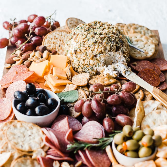 Ranch cheeseball recipe on a wooden cutting board with crackers, nuts, olives, grapes, and meats.