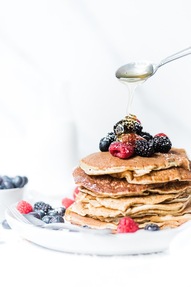 Protein pancakes on a white plate - with honey being poured on top.