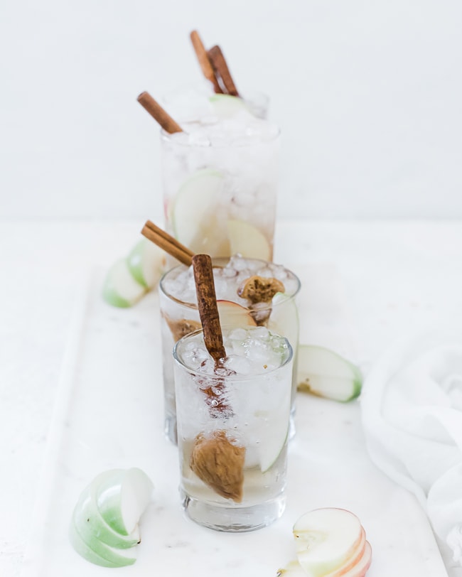 Apple pie fruit water recipe in glasses filled with ice atop a marble tray.