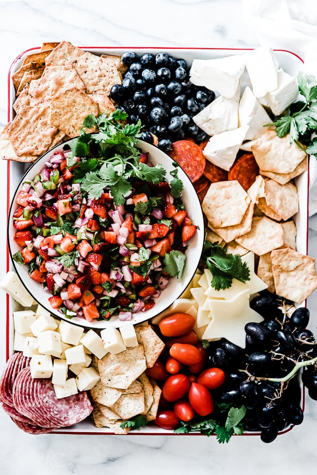 Strawberry salsa on a white tray surrounded by cheese and crackers.