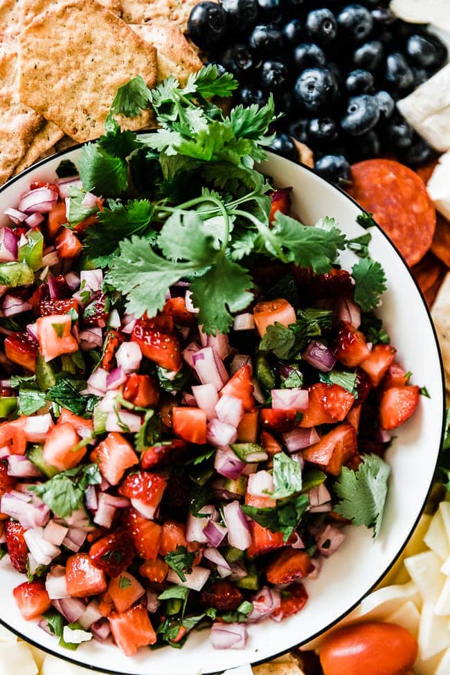 A closeup of strawberry salsa in a white bowl. There is cilantro as garnish to one side.