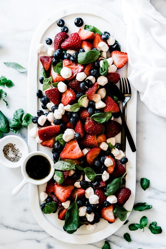 Summer strawberry salad on an oval marble tray. There is a bowl of dressing and a bowl of pepper to the side.