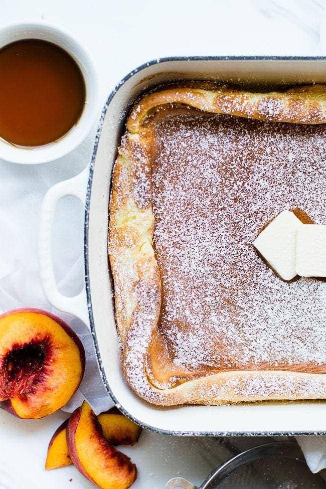 German pancakes with butter and powder sugar in a baking dish, syrup and peaches at the side