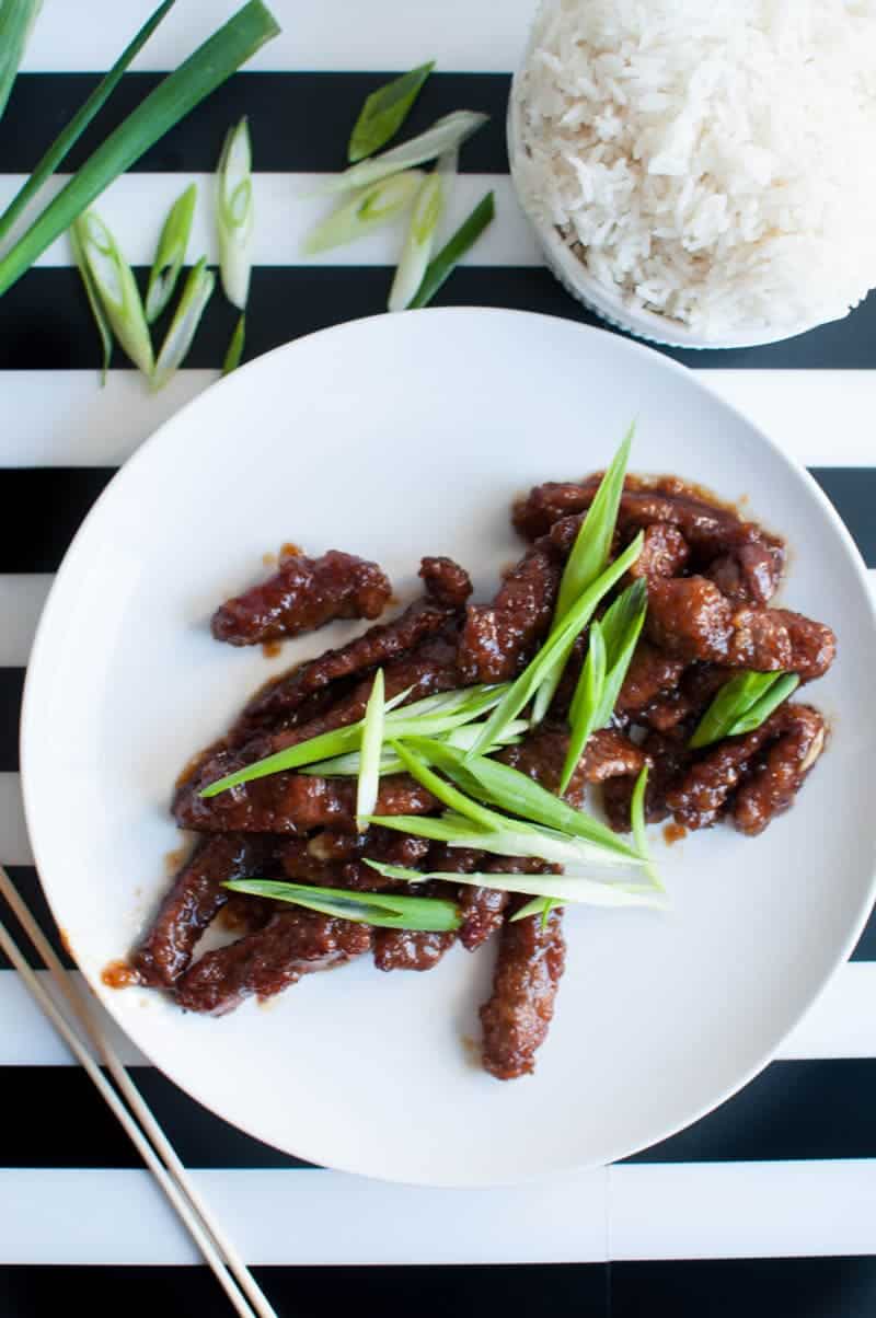 Mongolian beef on plate with a green onion garnish and a bowl of white rice on the side