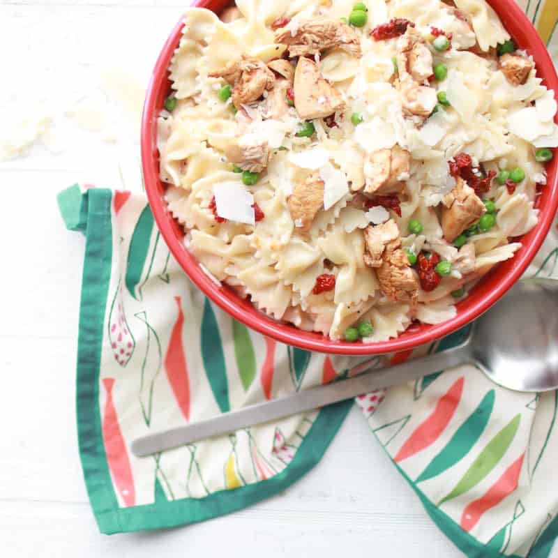 Bacon Chicken Pasta in bowl over fish patterned cloth with spoon next to it 