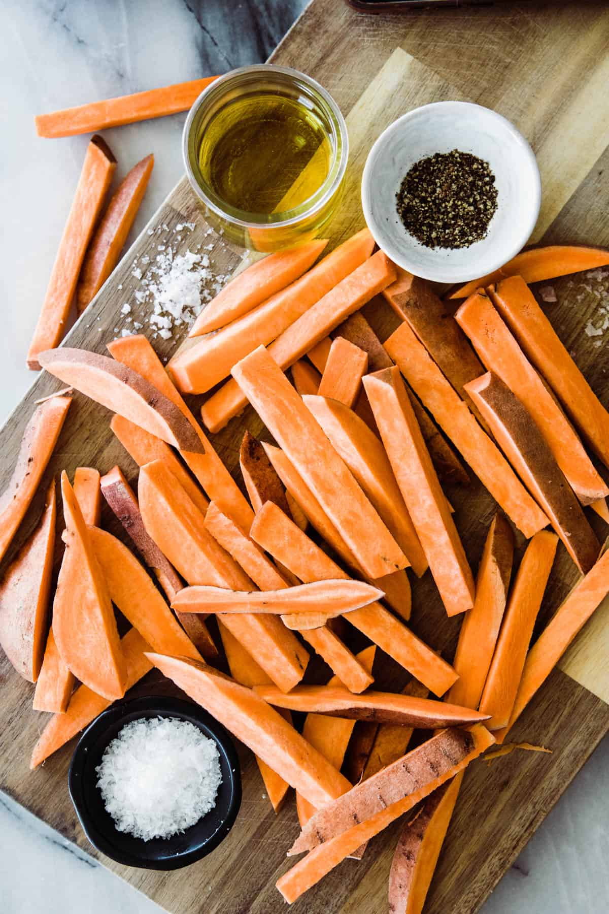 raw sweet potato fries, with oil, salt and pepper on cutting board. 