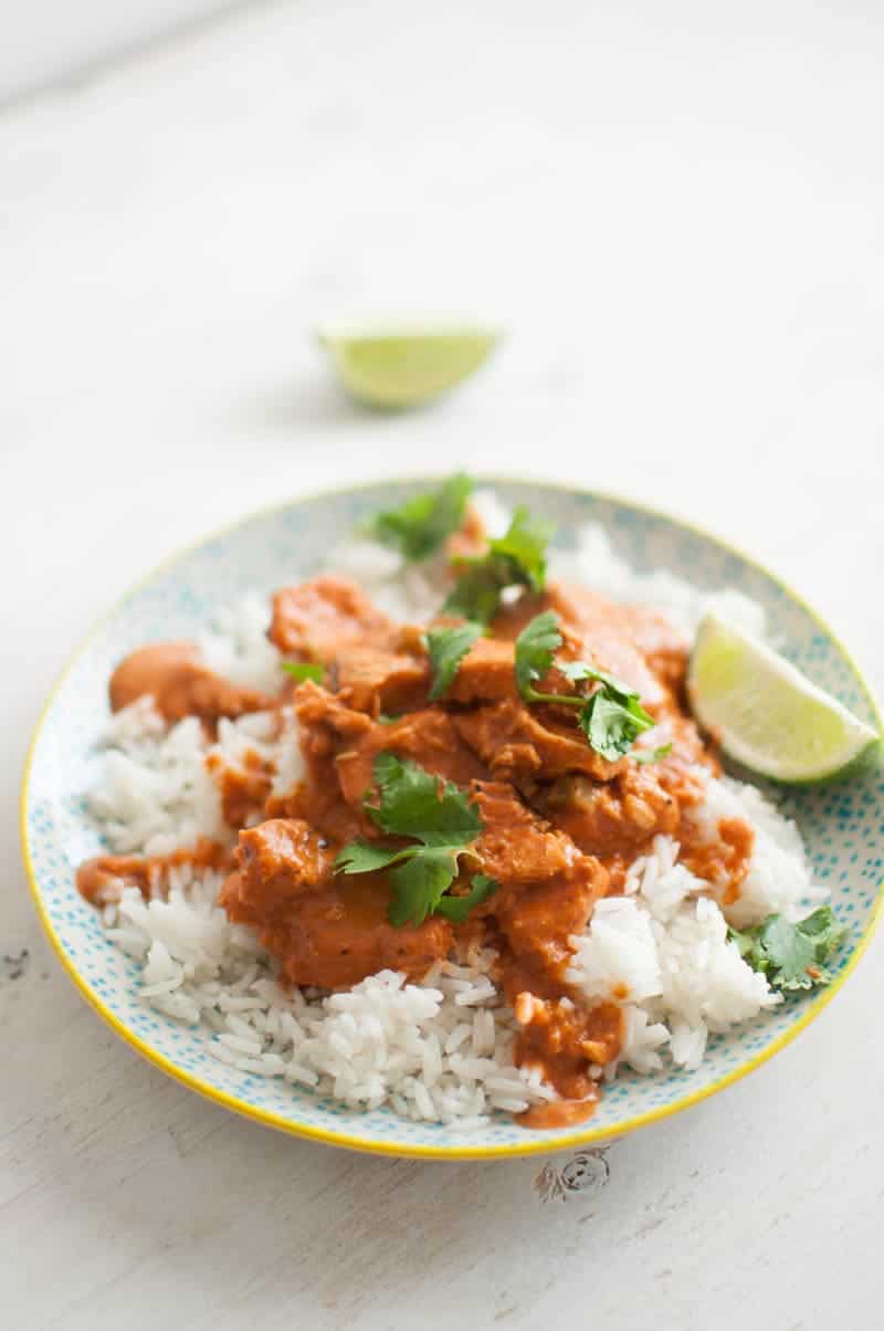 Chicken Tikka Masala on plate with green garnish and halved limes to the side 