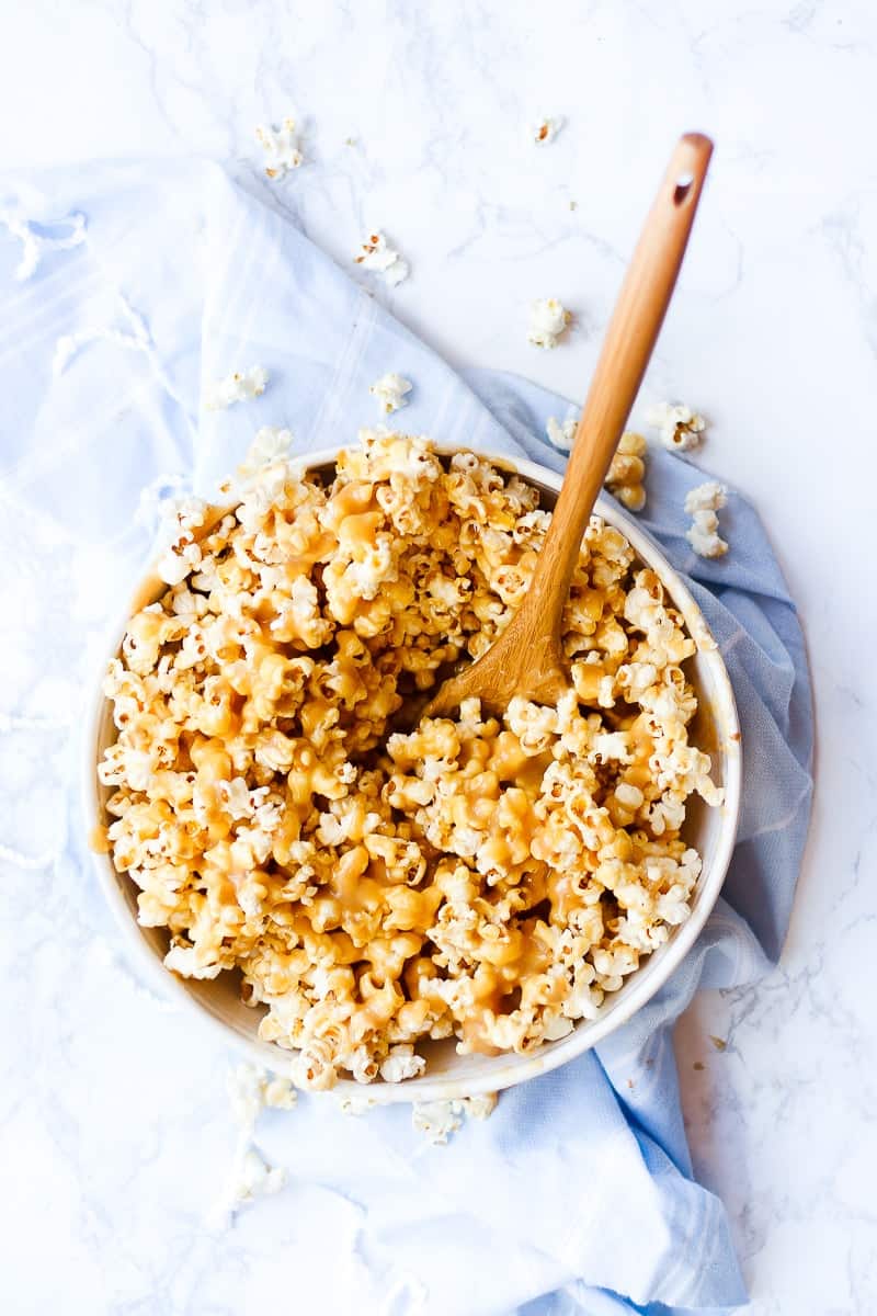caramel popcorn in a white bowl with a wooden serving spoon