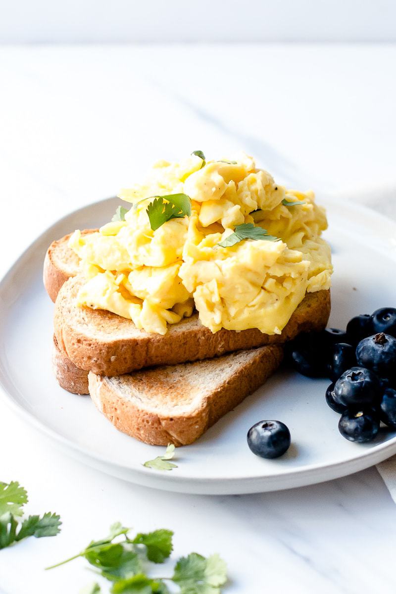 Slices of toast topped with The Best Scrambled Eggs and blueberries on the side