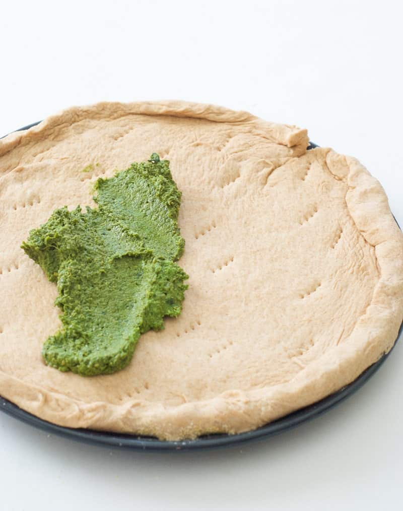 Greek Pesto being poured on pizza crust
