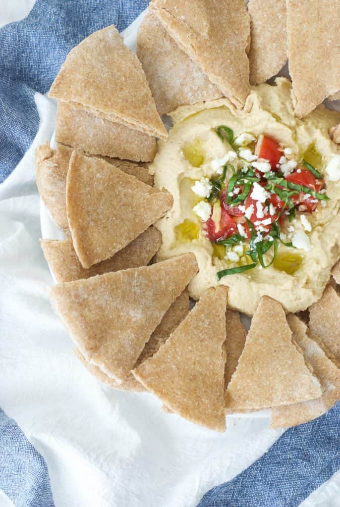 Hummus topped with veggies, on plate surrounded by triangle shaped  pita