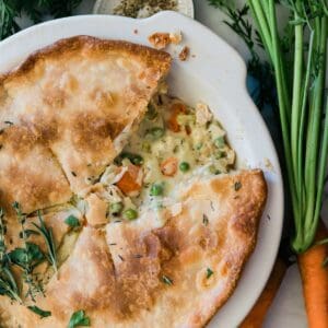 Homemade pot pie in a white pie pan. There are fresh carrots to the side.