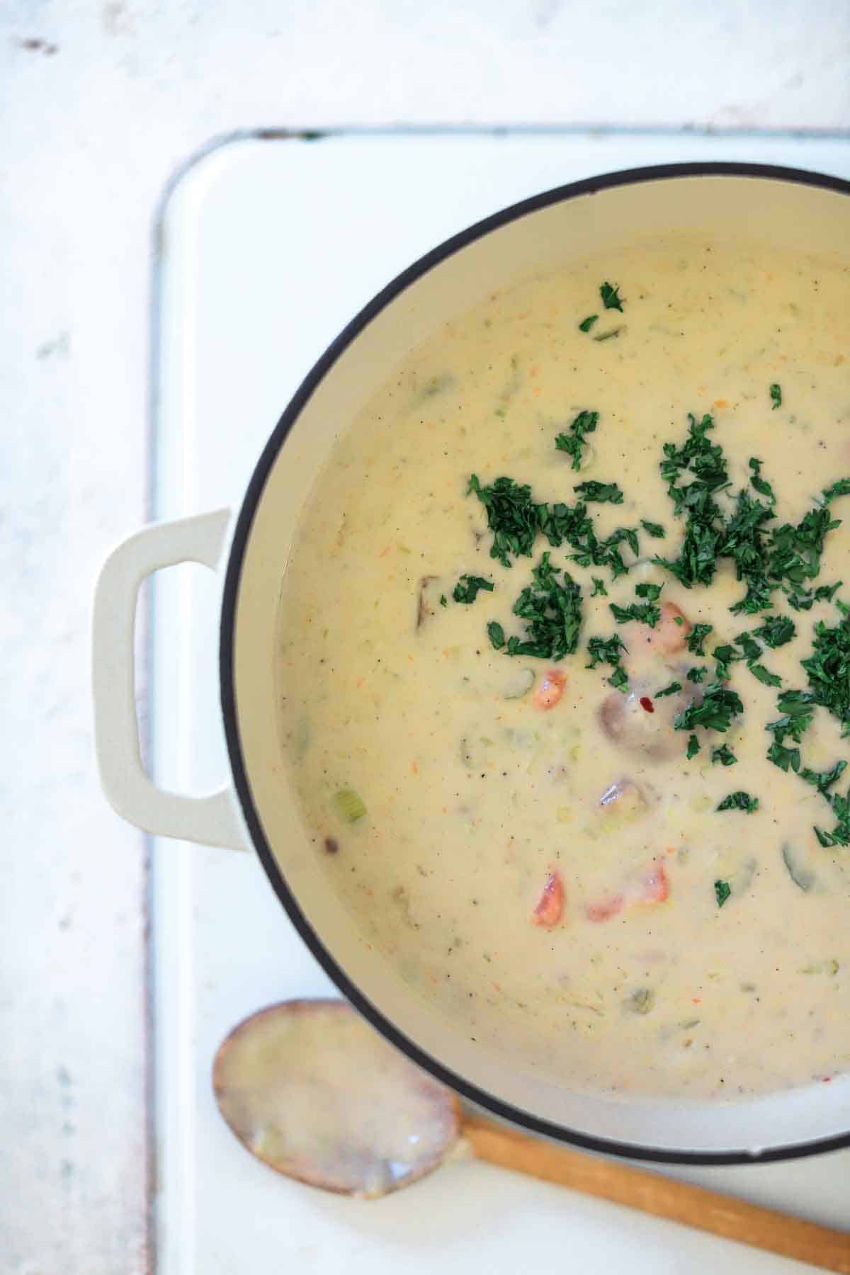 New england clam chowder in a pot with parsley on top and a spoon to the side.