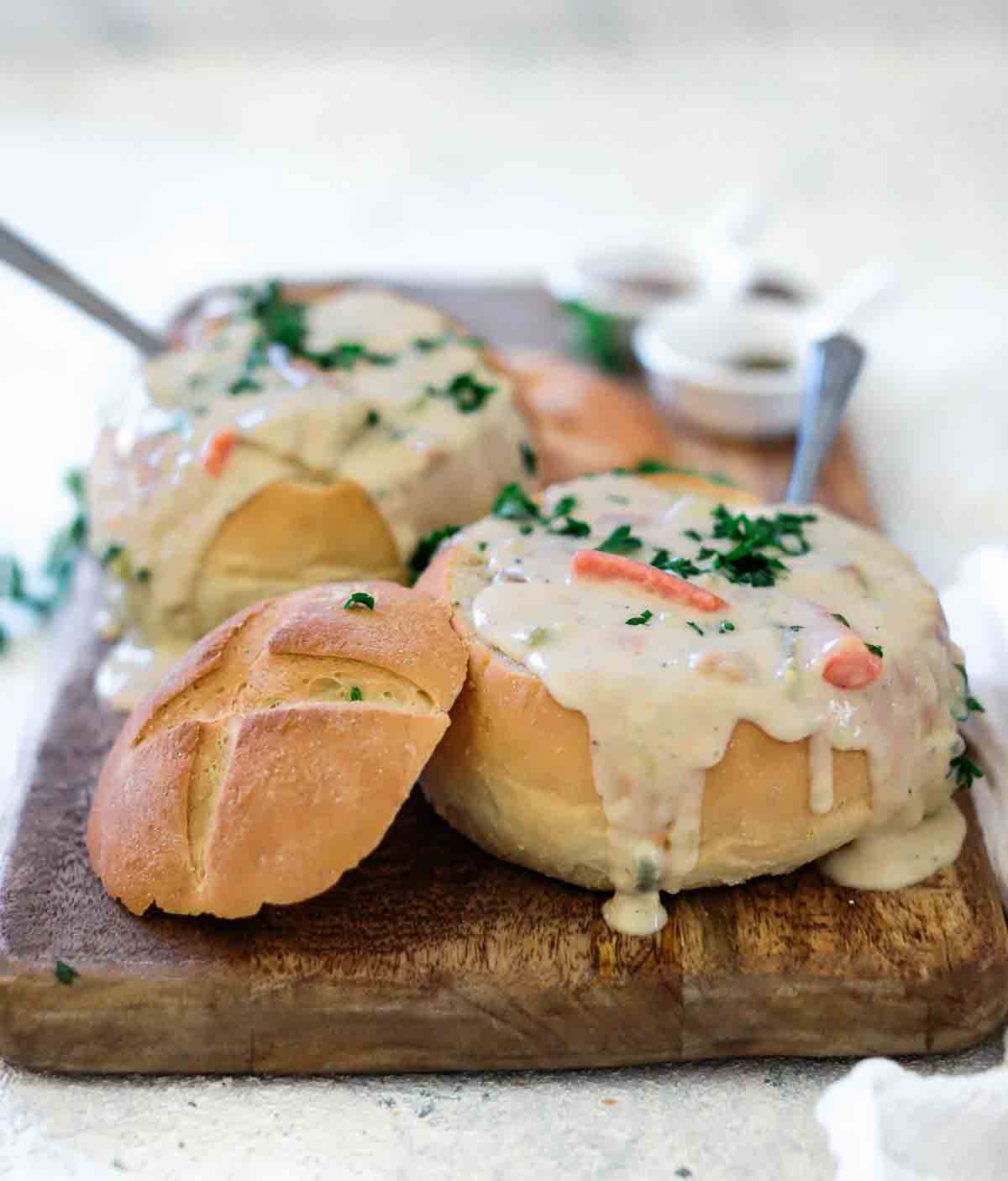 Boston clam chowder in bread bowls with spoons on a cutting board. 