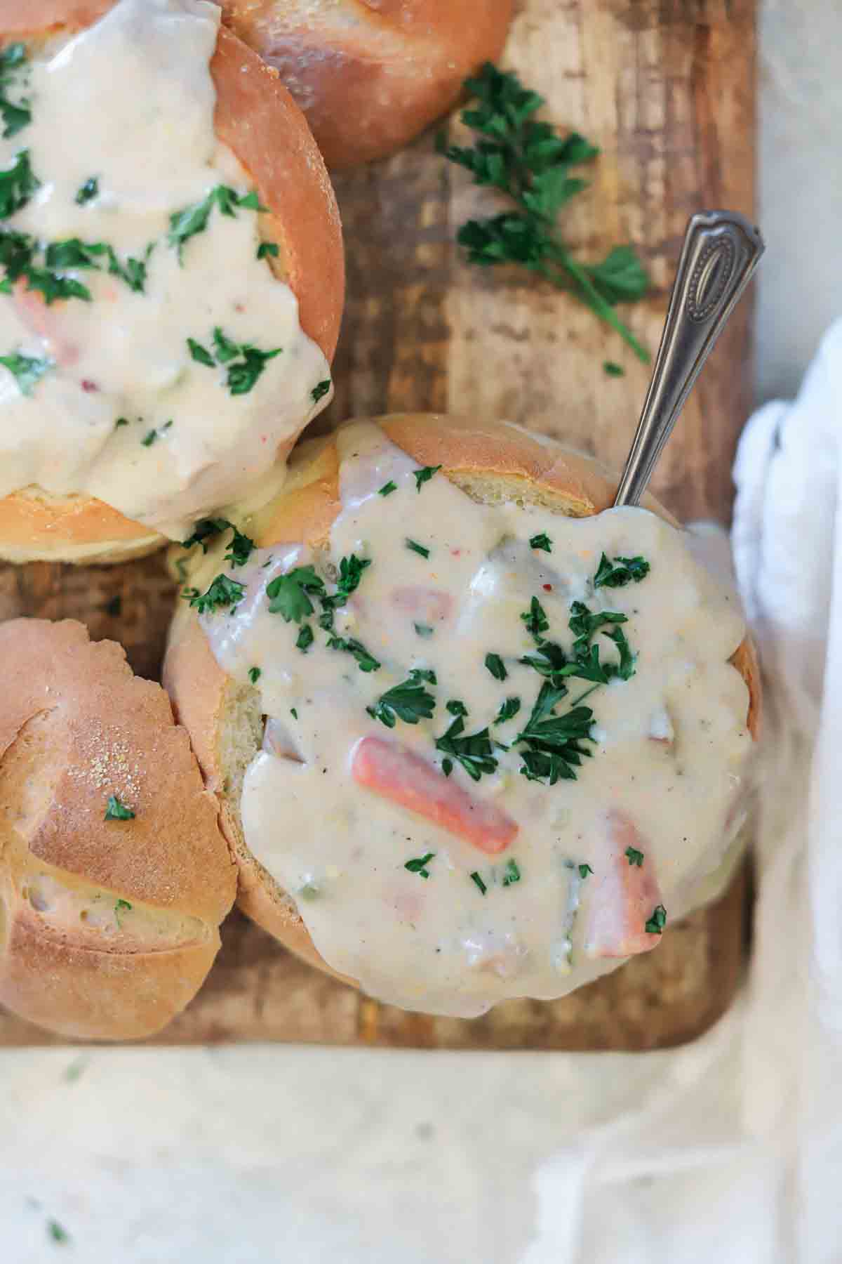 A close up shot of boston clam chowder in a bread bowl garnished with fresh parsley.