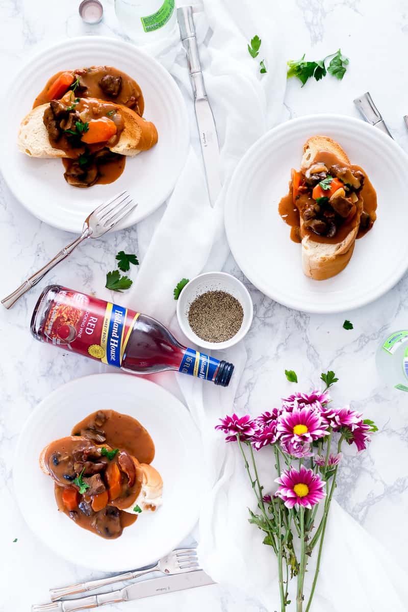 Slow Cooker Beef Bourguignon served on bread, red wine on table with flowers