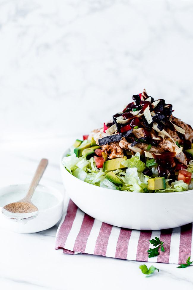 bbq chicken salad cpk in a white bowl with a red striped napkin and wooden utensils 