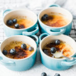 Vanilla Creme Brûlée is aqua cocottes on a wire cooling rack, garnished with berries.