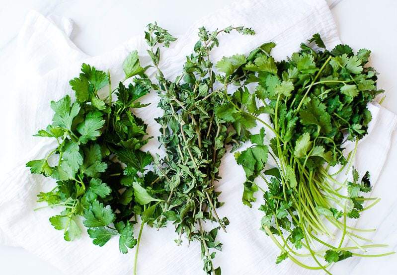 Three herbs used to make Chimichurri sauce on a white surface