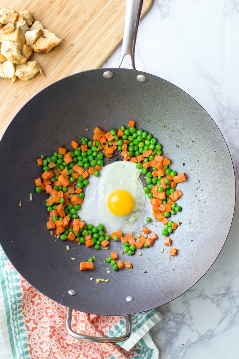 egg and peas and carrots in skillet with cutting board with chicken to the side