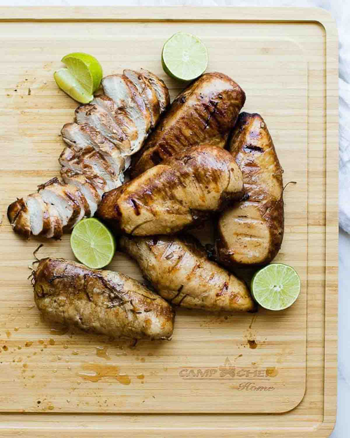 Cooked breasts in lime chicken marinade whole and cut on a cutting board with lime halves.