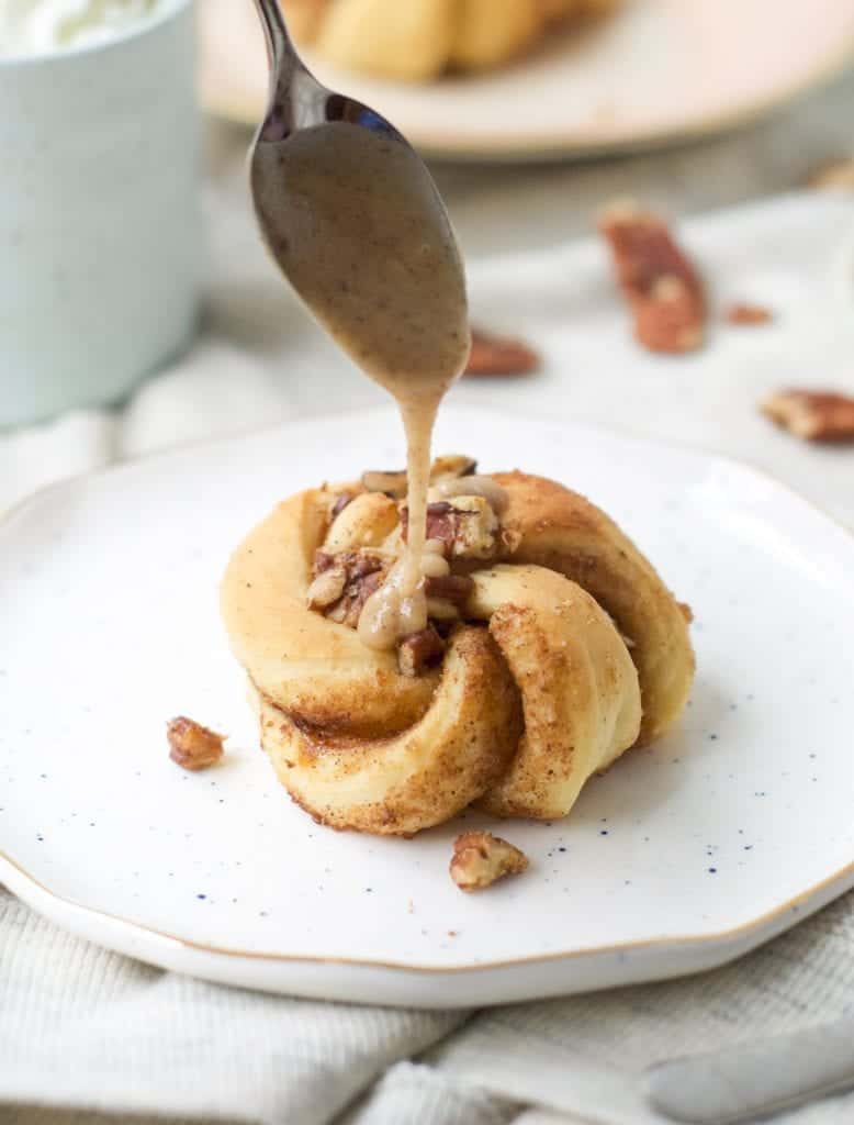 A close up of pecan coils on a white plate getting drizzled with brown butter icing