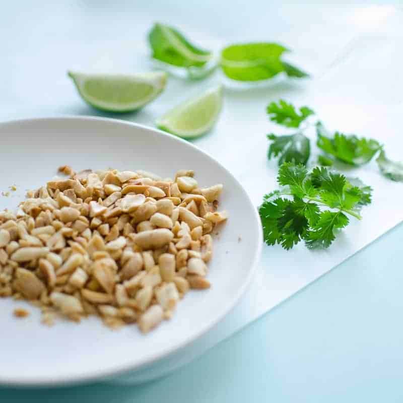 A close up of peanuts on a white plate with coriander as garnish used for topping a cabbage stir fry