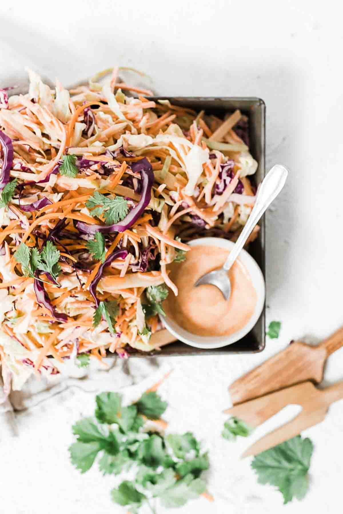 Homemade coleslaw recipe in a metal cake pan, dressing to the side.