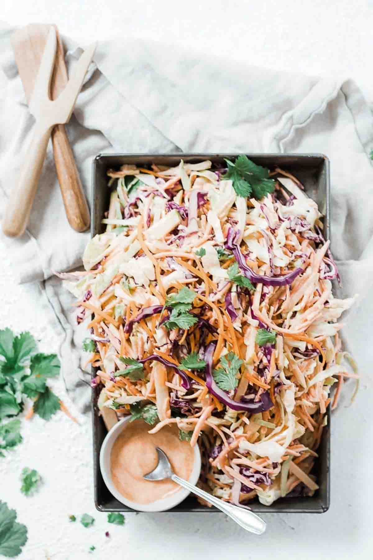 Homemade apple cabbage slaw recipe in a metal cake pan, dressing to the side.
