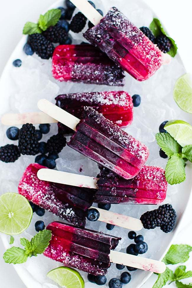 triple berry popsicles on a tray of ice with lime wedges