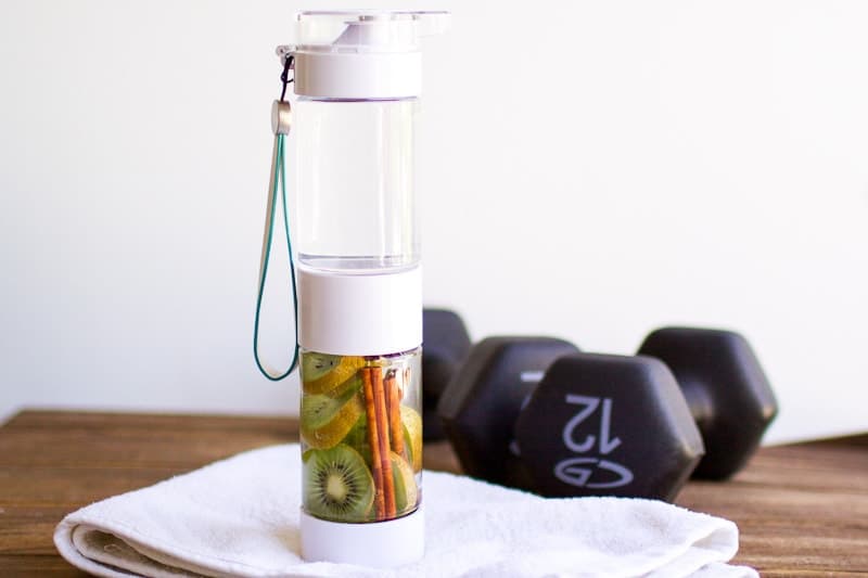 kiwi cinnamon infused water in bottle next to hand weights