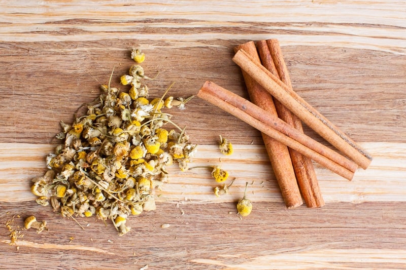 A pile of chamomile flowers and cinnamon sticks on a wooden surface