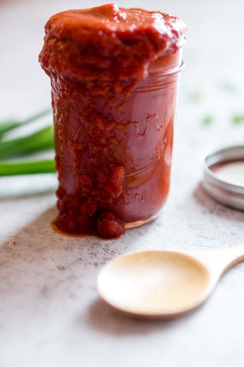 Homemade Red Enchilada Sauce in mason jar with a wooden spoon at the side