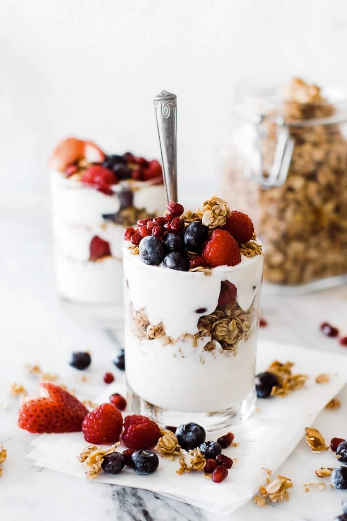 A glass of yogurt layered with berries and healthy granola and a jar of granola in the background.