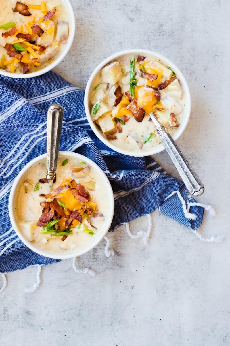 Baked Potato Soup in bowls with spoons. topped with cheese, onions, and bacon