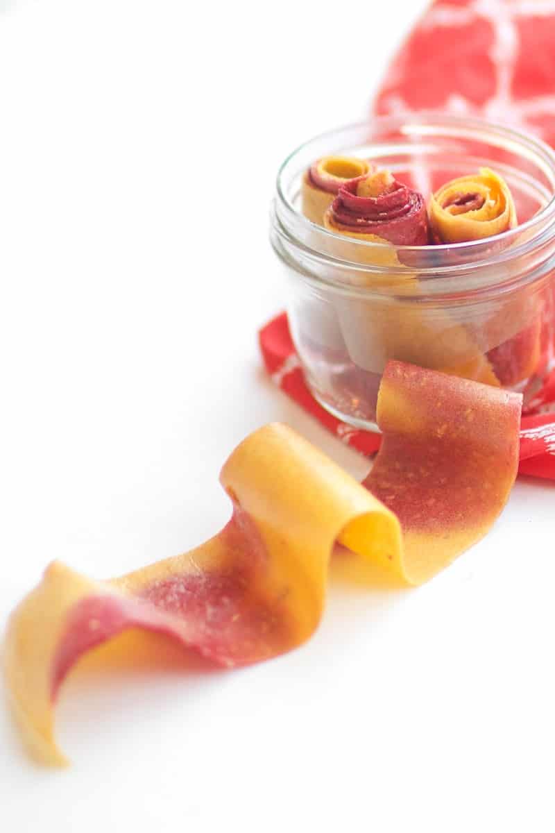Peach Raspberry Fruit Leather rolled up into a jar, and some stretched out across the table