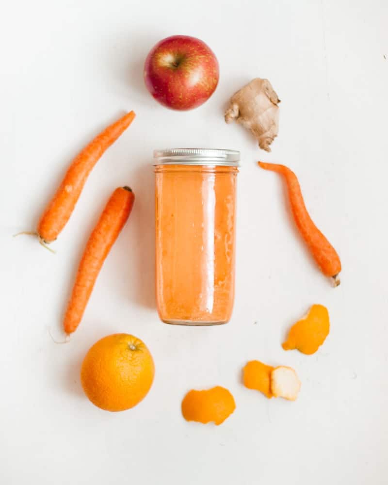 bright orange juice in jar, surrounded by its ingredients