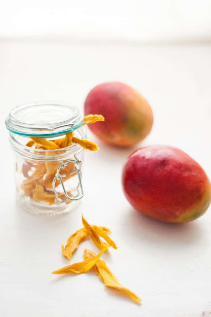 Dried mango in a glass jar with 2 mangoes at the side