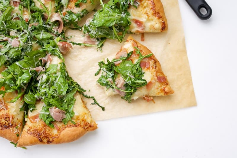 An overhead shot of a Prosciutto and Arugula Alfredo Pizza with a slice cut out