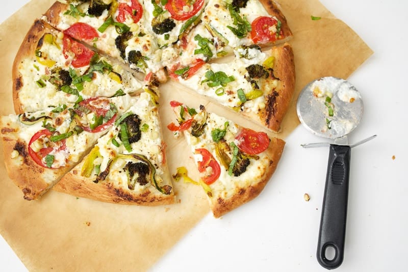An overhead shot of a ricotta pizza topped with vegetables and cut into slices