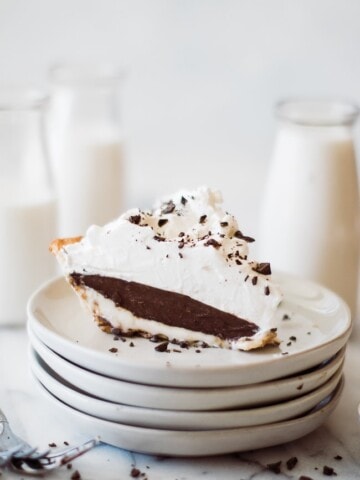 a slice of chocolate pie topped with whip cream on a stack of plates