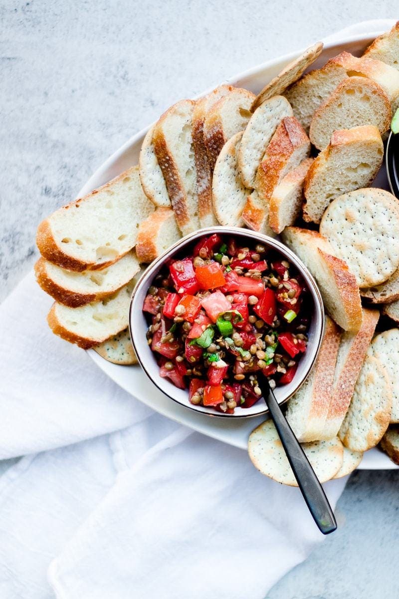 Lentil Bruschetta in a small bowl, surrounded by baguette pieces