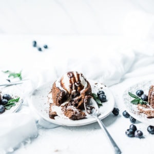 Molten Chocolate Cakes on white plates, garnished with vanilla ice cream and blueberries.