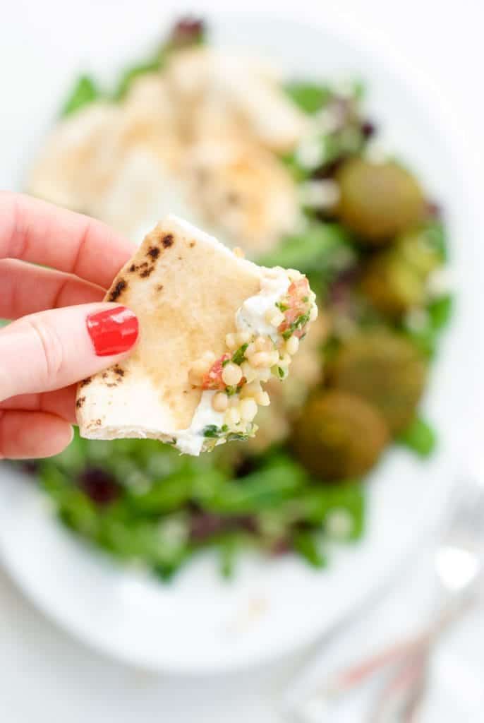 A hand holding a piece of pita bread with some Couscous Tabbouleh Salad
