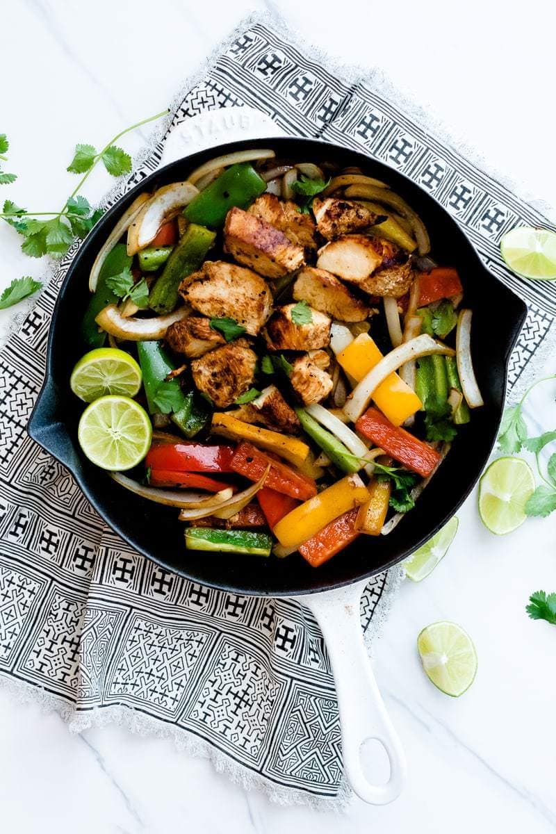Skillet Chicken Fajitas on patterned rag with cilantro and halved limes around