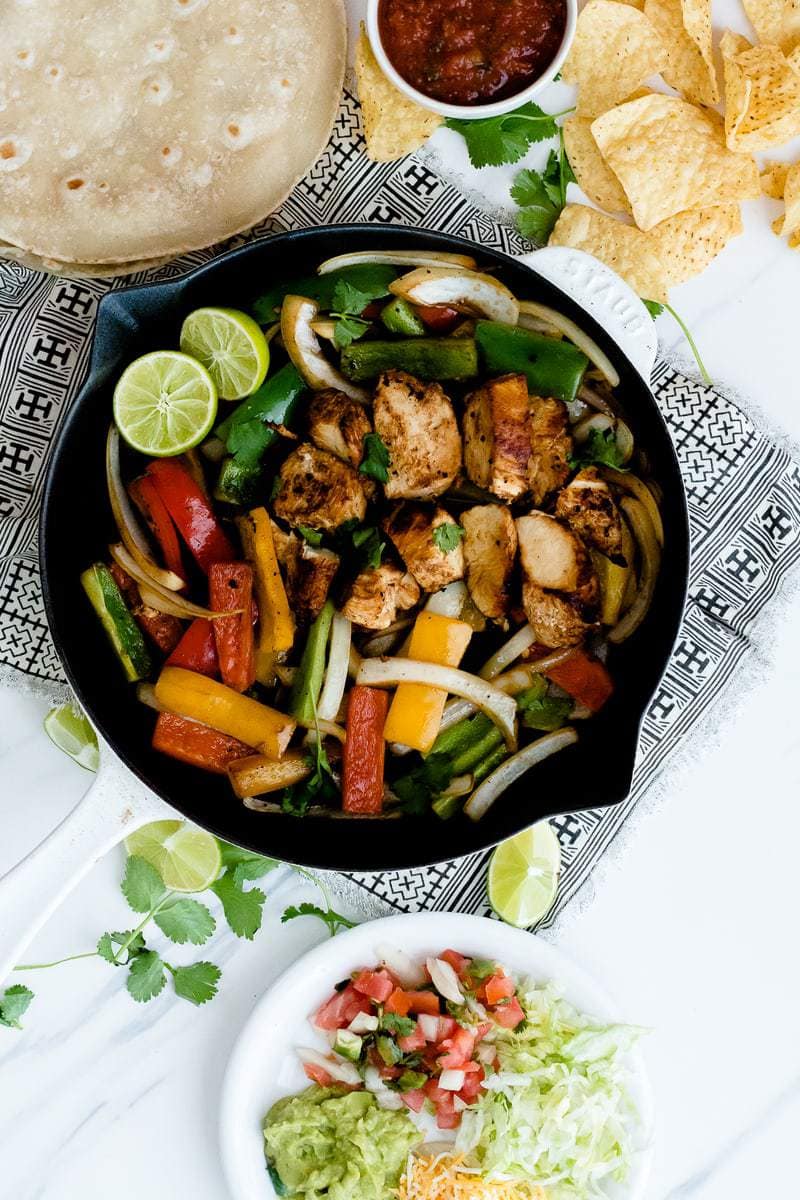 Skillet Chicken Fajitas next to plate of taco toppings and guacamole