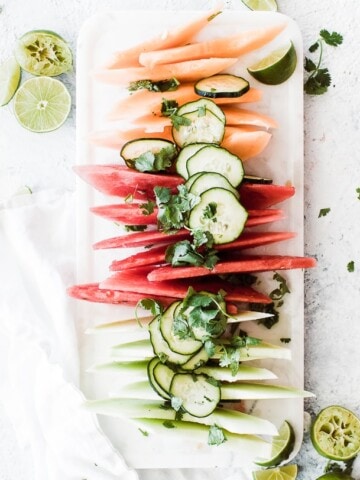 tray of melon slices and cucumber slices topped with lime juice and cilantro