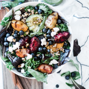 Stone fruit grilled salad in a white bowl, atop a wooden cutting board.