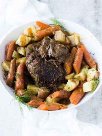 Instant pot roast beef in a white bowl with roasted vegetables