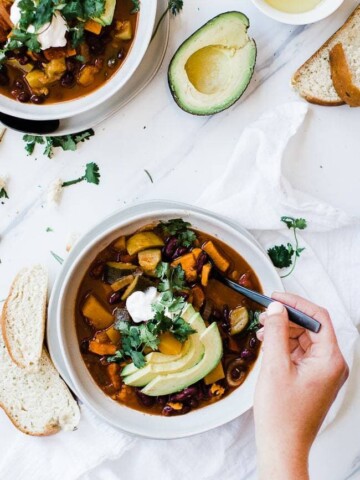 hand holding spoon in bowl of vegetarian chili with cilantro garnish and avocado